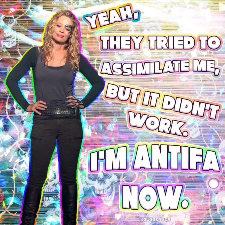 The meme features a photo of actress Jennifer Lawrence with a quote superimposed over her. The quote is from her 2013 interview with "The Daily Mail" and reads, "Yeah, they tried to assimilate me, but it didn't work. I'm Antifa now." The quote is presented in a playful, comic-book-like font with a rainbow-colored outline. The background of the image is a mix of skulls and other objects, giving it a somewhat edgy, subversive feel. Overall, the meme appears to be poking fun at the idea of antifascist (or "antifa") ideology and its association with radical or extreme views.   The image is meant to be humorous and satirical, rather than serious or political. It's likely intended to be shared and discussed on social media or other online platforms, where it can be seen by a wide audience. The use of a popular culture figure like Jennifer Lawrence and a catchy, attention-grabbing quote is meant to make the meme more shareable and engaging. Overall, the meme is a ligh-hearted and irreverent commentary on the idea of antifascism and its perceived association with radical or extreme views.